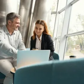 Älterer Mann der jüngerer Frau etwas auf seinem Laptop zeigt