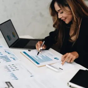 Frau die daten auf ihrem Tisch und ihrem Laptop analysiert